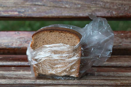 The forgotten black bread on a bench in a transparent plastic bagの写真素材