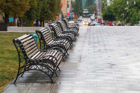 Row of five benches on the street in the rainy weatherの写真素材
