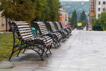 A row from five benches on the street in rainy weatherの写真素材