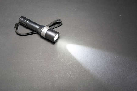 Glowing metal flashlight with wrist strap on a dark backgroundの写真素材