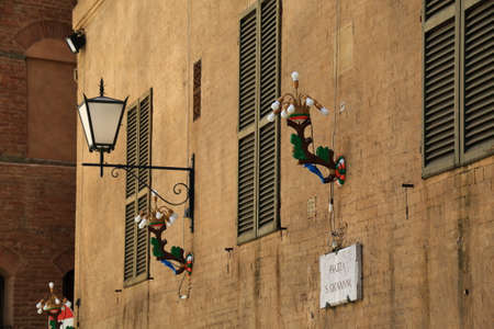 Siena, Italy - August 20, 2015: Street light on a yellow wall with windows in Piazza S. Giovanniのeditorial素材