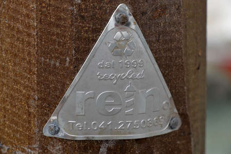 Venice, Italy - August 21, 2015: Aluminium triangle on wooden column mounted in water of the venetian canal with logo "dal 1999 recycled Rein Tel.041.2750369"のeditorial素材