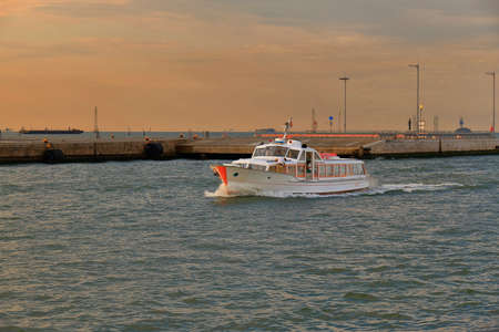 Venice, Italy - August 21, 2015: Sailing white passenger motorboat in port of Venice at sunrise