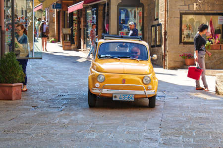San Marino, Italy - August 22, 2015: Old yellow car Fiat 500 in the street with people in San Marino
