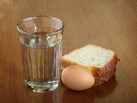 A full glass of water, egg and two slices of bread on an scratched brown wooden table. Concept of...