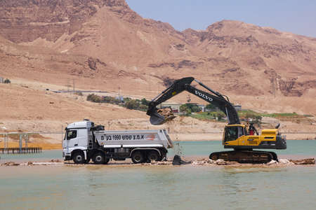 Ein Bokek, Israel - June 10, 2017: Excavator scooping soil from the bottom of the Dead Sea and put into the truck for extraction of mineralsのeditorial素材