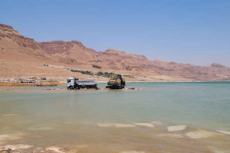 Ein Bokek, Israel - June 10, 2017: Excavator scooping soil from the bottom of the Dead Sea and put into the truck. Mining of mineralsのeditorial素材