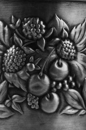 Details of an old metal cup holder, decorated with a bas-relief depicting leaves, cherries and...