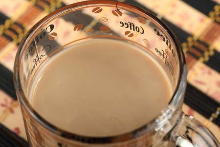 Full transparent glass cup with coffee and milk on a bamboo table mat in cafe. Top view close-up