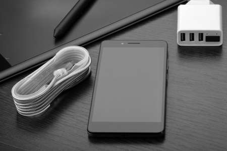 Smartphone, white charger with three USB ports and display, cable and graphic tablet with stylus on...