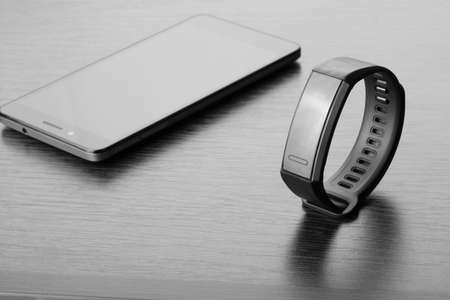 Activity tracker (fitness tracker) and smartphone on a dark wooden table. Monochrome image