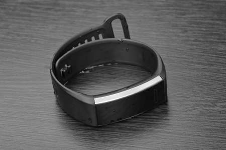 Activity tracker, also known as a fitness tracker on a dark wooden table. Monochrome image