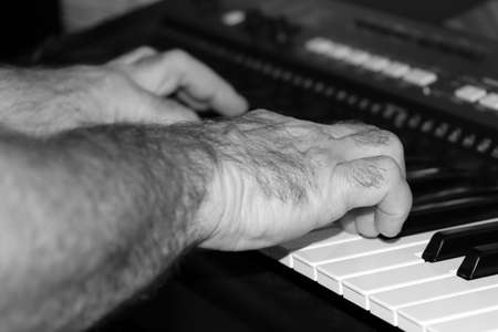 Male hands of a musician who plays music on a synthesizer. Monochrome image