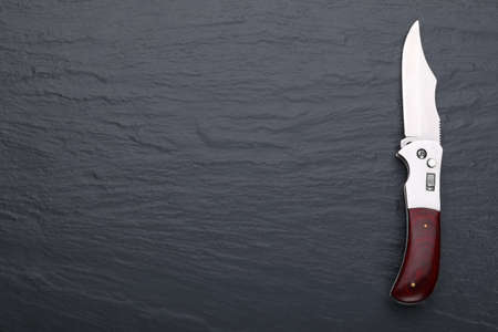 Steel folding knife with an open blade on a stone surface. Copy space. Steel arms. The concept of...