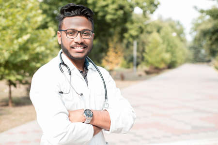 portrait of a young handsome indian doctor wearing glasses. A guy in a white coat with a...