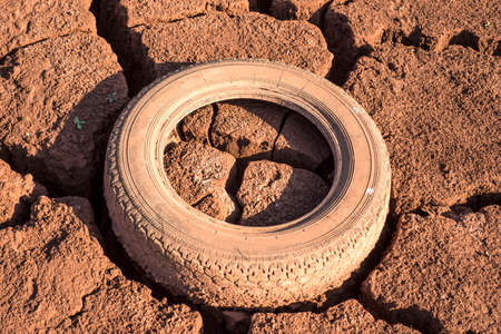 rubber pollution. Old car tires, wheels, in the old dry cracked earth, close-up. Environmental pollution by rubber, engine wheels, on the coast of a lake. The earth is saturated with red ore. Texture closeup car tireの写真素材