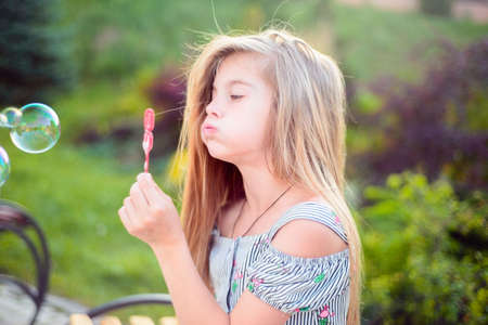 Portrait of a beautiful little girl blowing soap bubbles. A child plays with bubbles, on a green background. Outdoorの写真素材