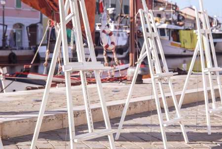 Easels for artists, against the backdrop of the canal and yachts, in the Italian province....