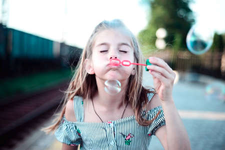 Portrait of a beautiful little girl blowing soap bubbles. A child plays with bubbles, on a green background. Outdoorの写真素材