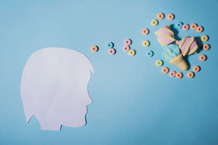 illustration of a diet violation. The face of a man made of paper, on a blue background, shows thoughts of sweets, and sweets. Thinks and dreams of sweets. Junk foodの写真素材