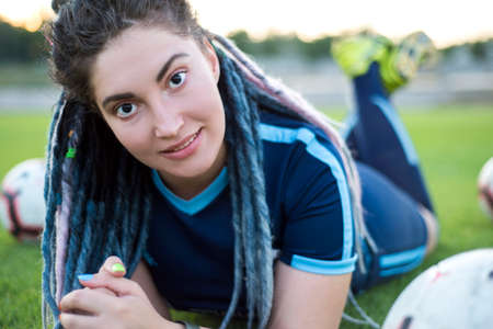 portrait of a young smiling girl. Woman with dreadlocks, on green grass field, with soccer balls,...