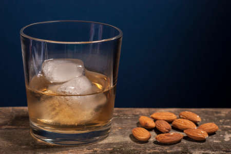 glass of whiskey, scotch tape, on wooden background. Almonds and hazelnuts are nearby.の写真素材