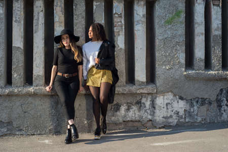 a girl in a leather jacket and a white sweater, a girlfriend in black jeans and a black hat, young Mexican girls at the textured wall, sister's day. Fashion shootingの写真素材