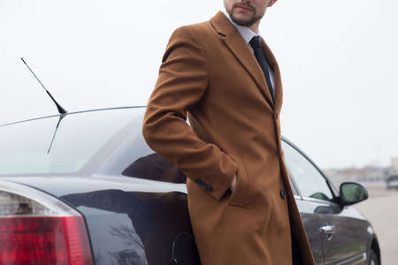 portrait of a young guy, a businessman in a stylish business suit, with a thump, stands by the car....