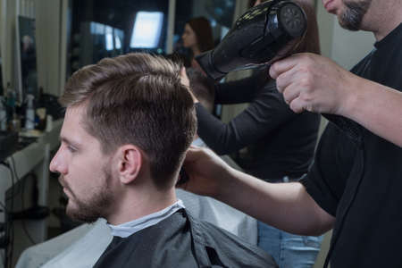 Close-up. Master hairdresser blow-drys a young guy in a barbershop. Care for men's hair. Men's beauty. Haircut and hair stylingの写真素材