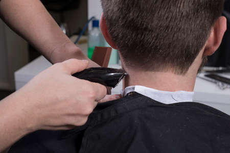 Hairdresser cuts hair with a trimmer for a young guy with a beard. Close-up of a master haircutting male hair. Cutting hair at the temples of a guy. Bearded man at the hairdresser. Men's haircutの写真素材