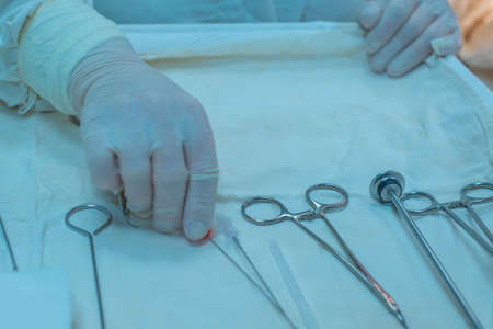 close-up, hands of a surgical nurse taking medical instruments from a sterile table, against the background of a team of doctors, doing the operation. Work in a sterile operating room. Item table for tools. The medicine. Close-up surgeryの写真素材