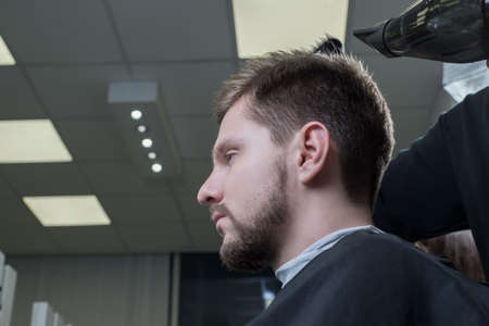 Close-up. Master hairdresser blow-drys a young guy in a barbershop. Care for men's hair. Men's...