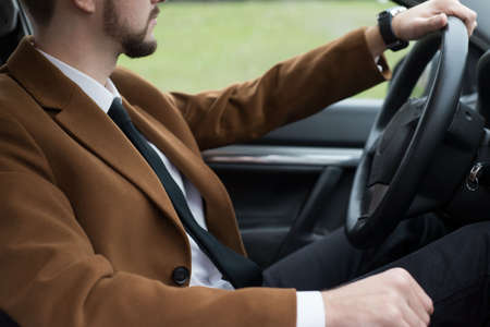 portrait of a young bearded guy in a suit driving a car. Business man in a coat and white shirt with a tie. Businessmanの写真素材