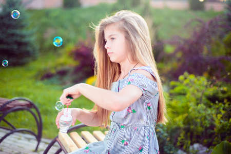 Portrait of a beautiful little girl blowing soap bubbles. A child plays with bubbles, on a green background. Outdoorの写真素材