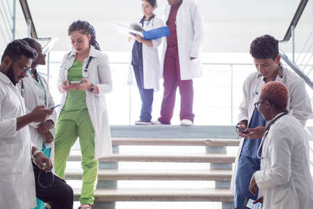 young doctors, mixed race, sitting, standing on the steps, in the corridor of the hospital. They consider x-rays, use gadgets to work in medicine. People in medical clothes.の写真素材