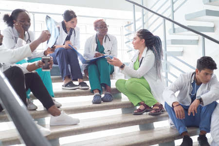 young doctors, mixed race, sitting, standing on the steps, in the corridor of the hospital. They consider x-rays, use gadgets to work in medicine. People in medical clothes.の写真素材