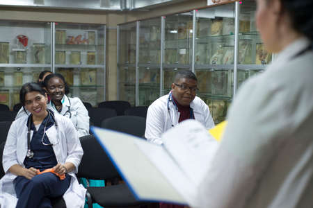 doctors, mixed race, in the classroom, at a medical conference. Young people, in white coats, with stethoscopes, are studying medicine. Classroom, anatomical museum. Students raise their hand to answer the question of the teacher, professorの写真素材