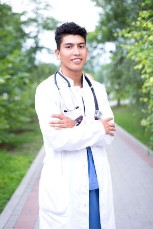 Portrait of a young handsome mexican doctor. A guy in a white coat with a stethoscope. Outdoor inの写真素材