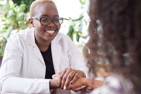 black woman doctor smiling holding mexican patient hand Mixed race young people at the doctors officeの写真素材