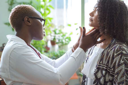 A black girl doctor examines a Mexican patient in a doctors office Palpates the lymph nodes of the neckの写真素材