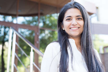 portrait of a beautiful young indian girl. Looks at the smartphone, smiles. Business lady doing businessの写真素材