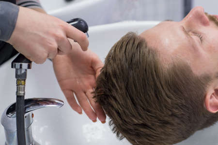 close-up of a male hair care master, washes a mans head in a sink after cutting his hair. Professional male hair care in barbershop.の写真素材