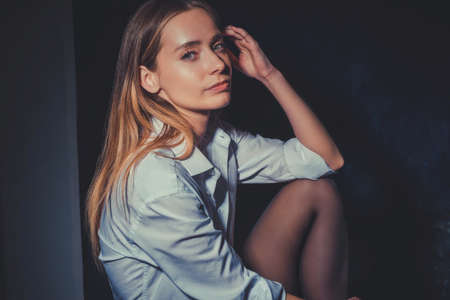 art portrait of a beautiful young girl, twenty-seven years old. The concept of tenderness and light exhibitionism, on a dark background, showing his shoulder, wearing a shirt. Erotic background, girl with a tattoo. Studio shooting art portrait of a young woman. Beautiful eyes. Tenderness and ease. Lonely girl. The look of a girl from the dark. Fashionable shooting. Creative tinting. Warm skin tintingの写真素材