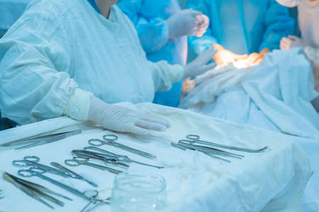 close-up, hands of a surgical nurse taking medical instruments from a sterile table, against the...