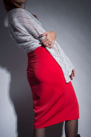 promotional photo of a female red skirt for a catalog, on a gray background. Girl in a red skirt showing sexy hipsの写真素材