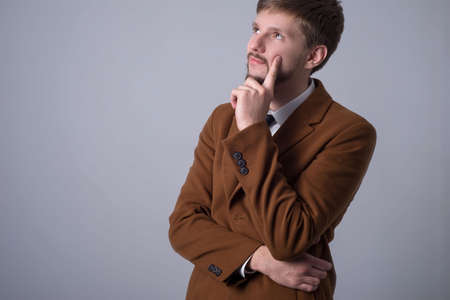 Portrait of a business man in a suit, a bearded dreaming man holds his hand near his chin, dreams, looking up. On a gray backgroundの写真素材