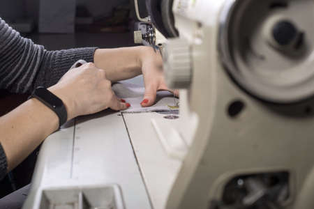A close-up of the hands of a seamstress sewing clothes sews fabric behind a sewing machine....