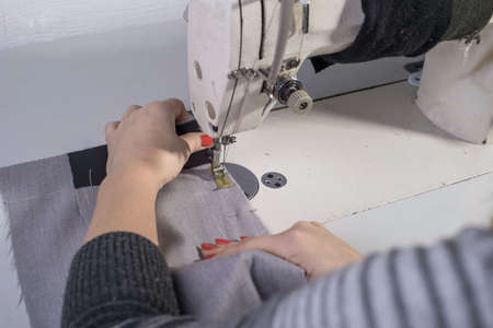A close-up of the hands of a seamstress sewing clothes sews fabric behind a sewing machine....