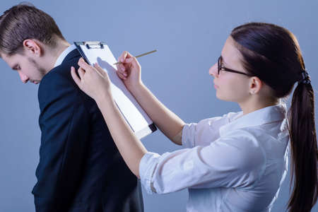 Portrait of two young businessmen, in business clothes, a subordinate man, framed his back as a background for a business woman to sign documents. Studio photo on a gray backgroundの写真素材