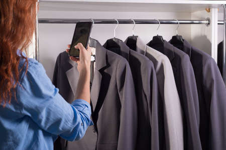 counter with business jackets in a clothing store. Free space. Shop of men's and women's business suits. Clothes sale girl using a smartphone photographs a counter with quality business jackets in a clothing storeの写真素材